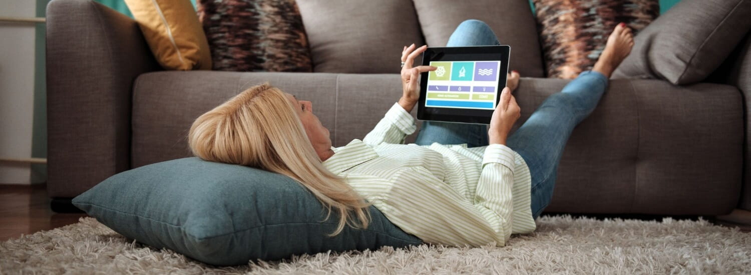 Woman lying on rug with her feet propped up on the sofa using tablet